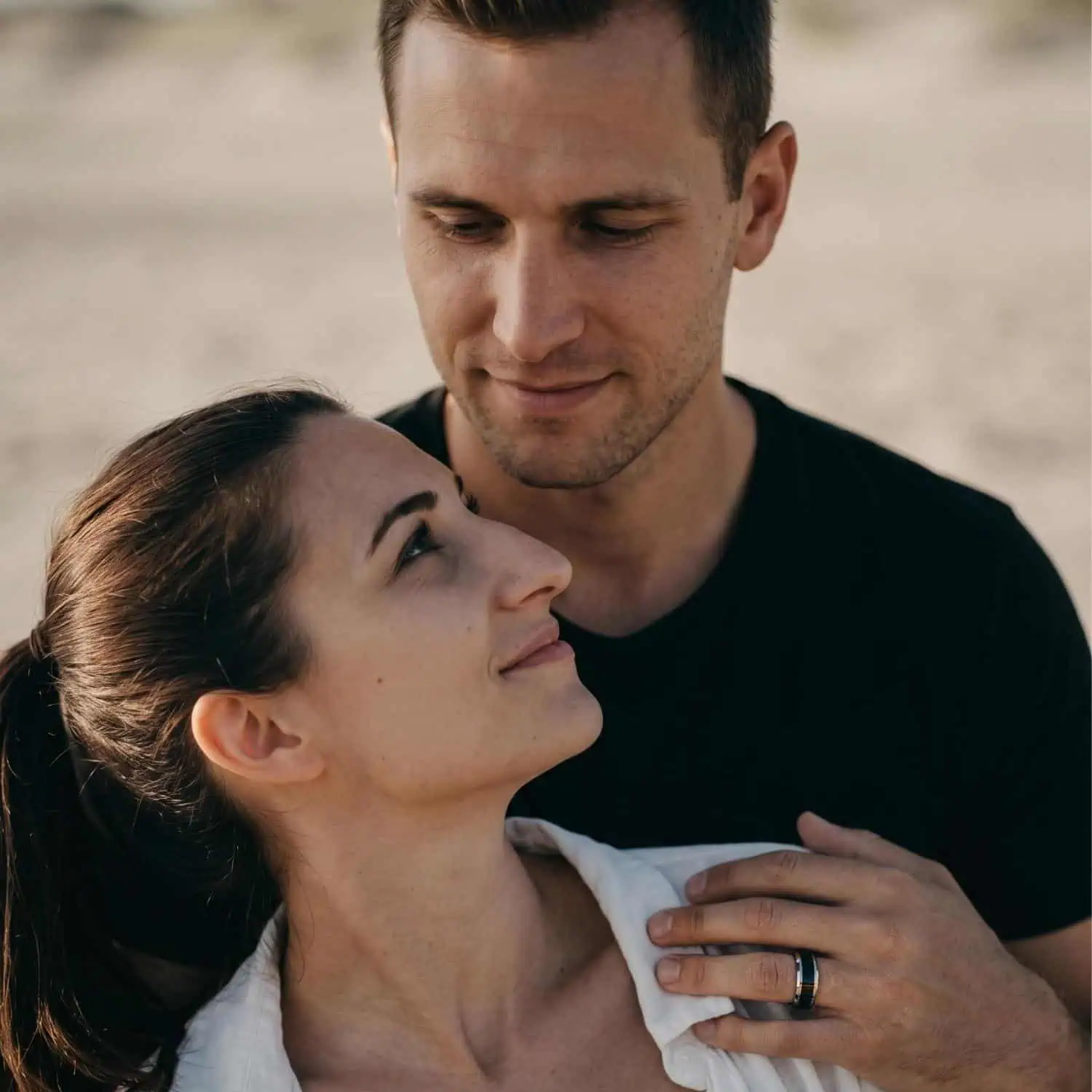 Couple smiling together as the man wears the Veritas silver tungsten wedding band while gently resting his hand on his partner's shoulder.