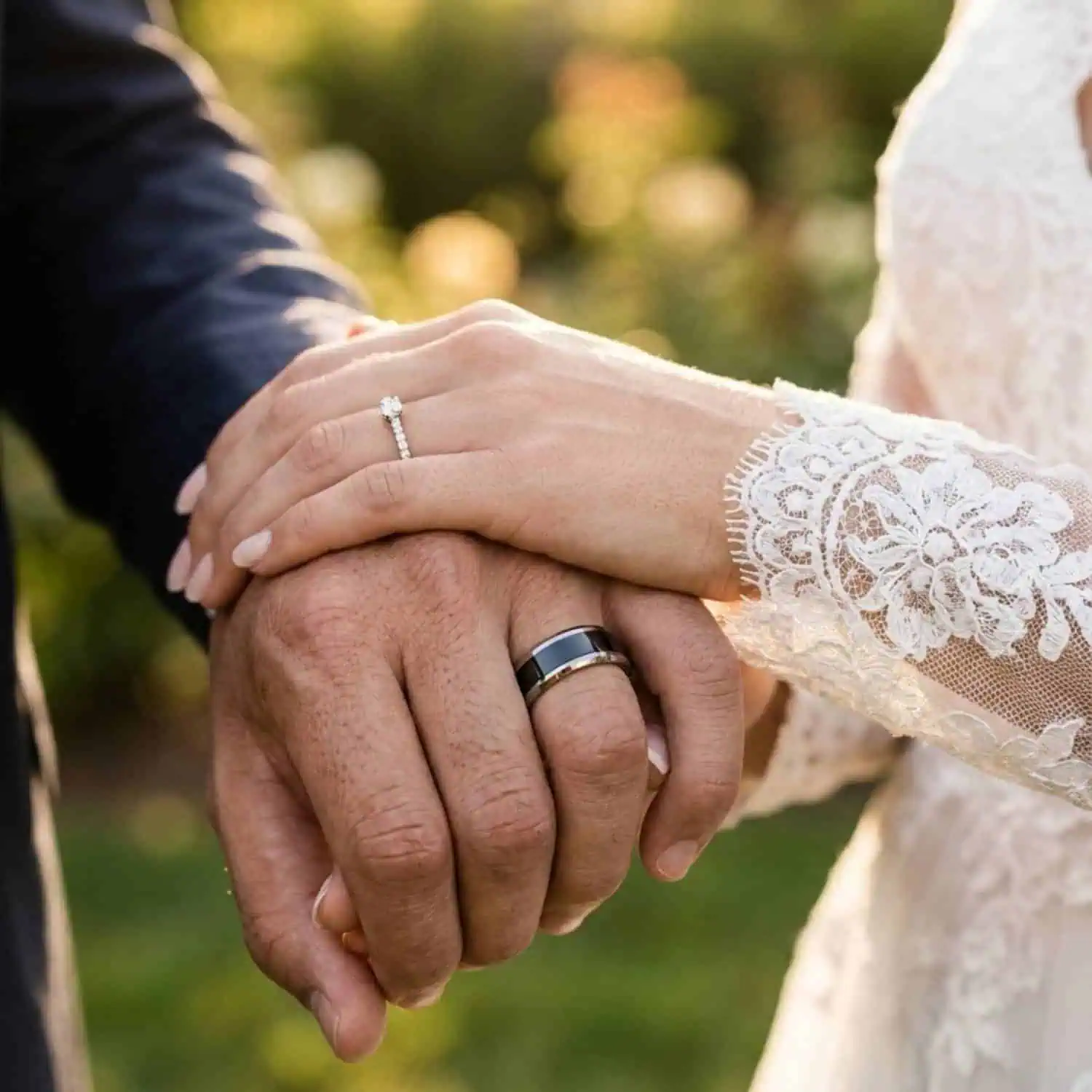 Newly married couple holding hands in a garden after their wedding, with the groom wearing the Veritas silver and black tungsten wedding band.