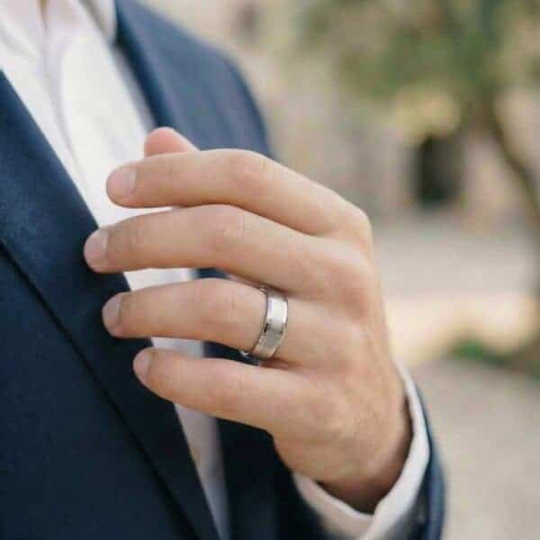 Dressed smartly in a navy suit, the man holds his hand to his chest. On his wedding finger is a white gold tungsten ring.