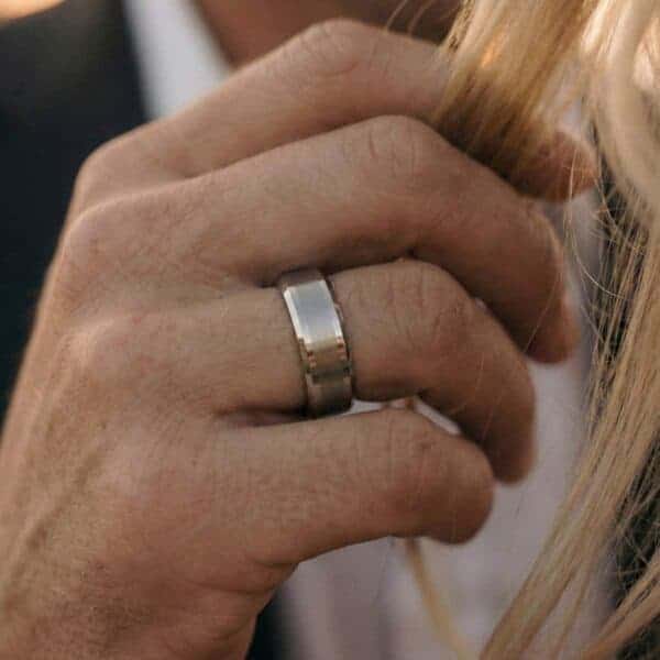 A close up of a mans hand who it gently holding his partners hair. On his hand, he wears a white gold tungsten ring.