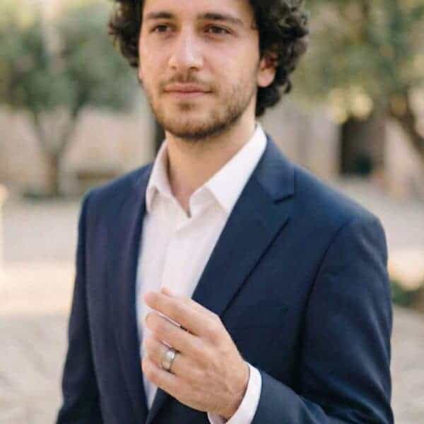 Facing the camera, a young man holds up his hand in front of him. He is wearing a white gold tungsten ring.