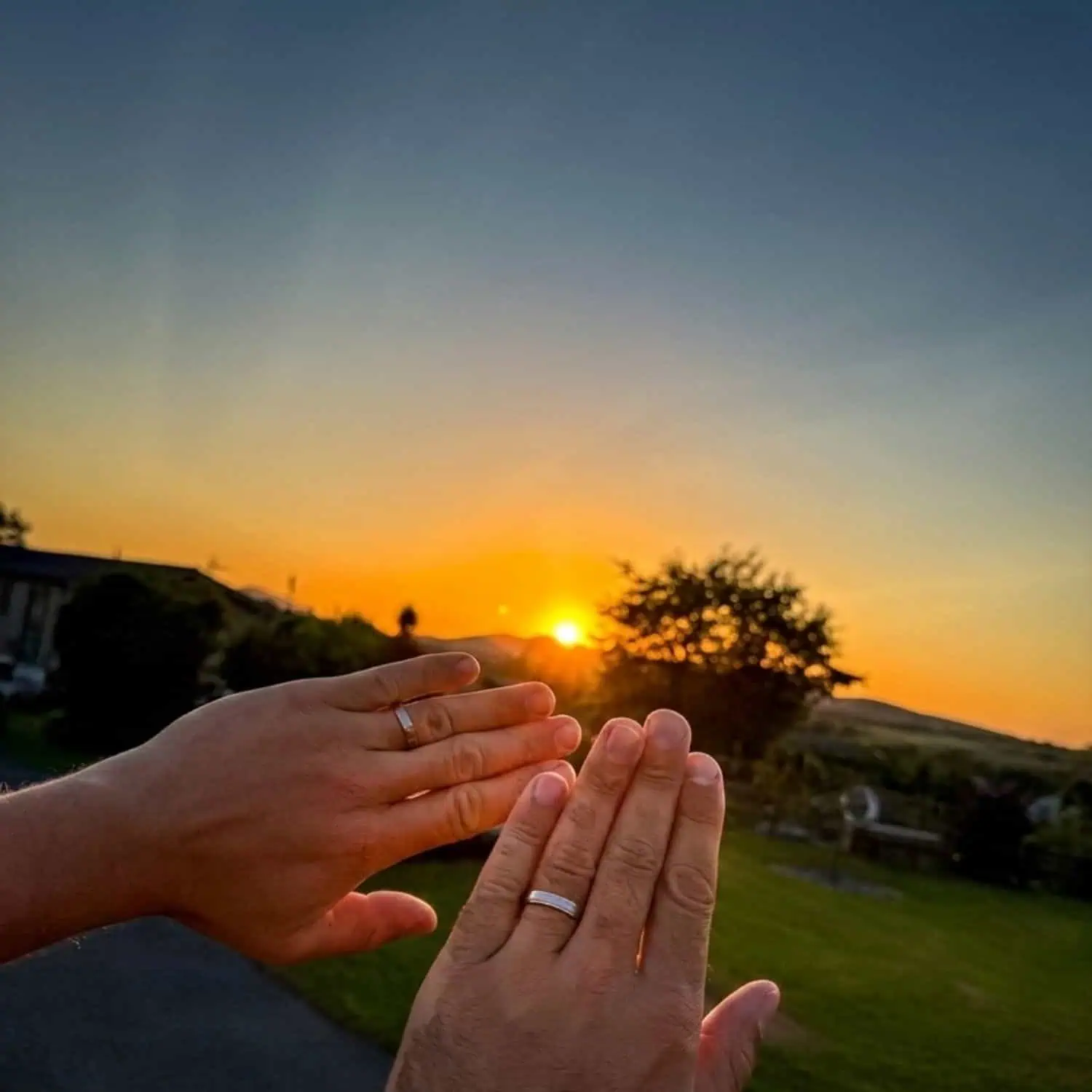 Couple holding out their hands at sunset, wearing matching Titan Thin Style titanium wedding rings with brushed silver raised centres.