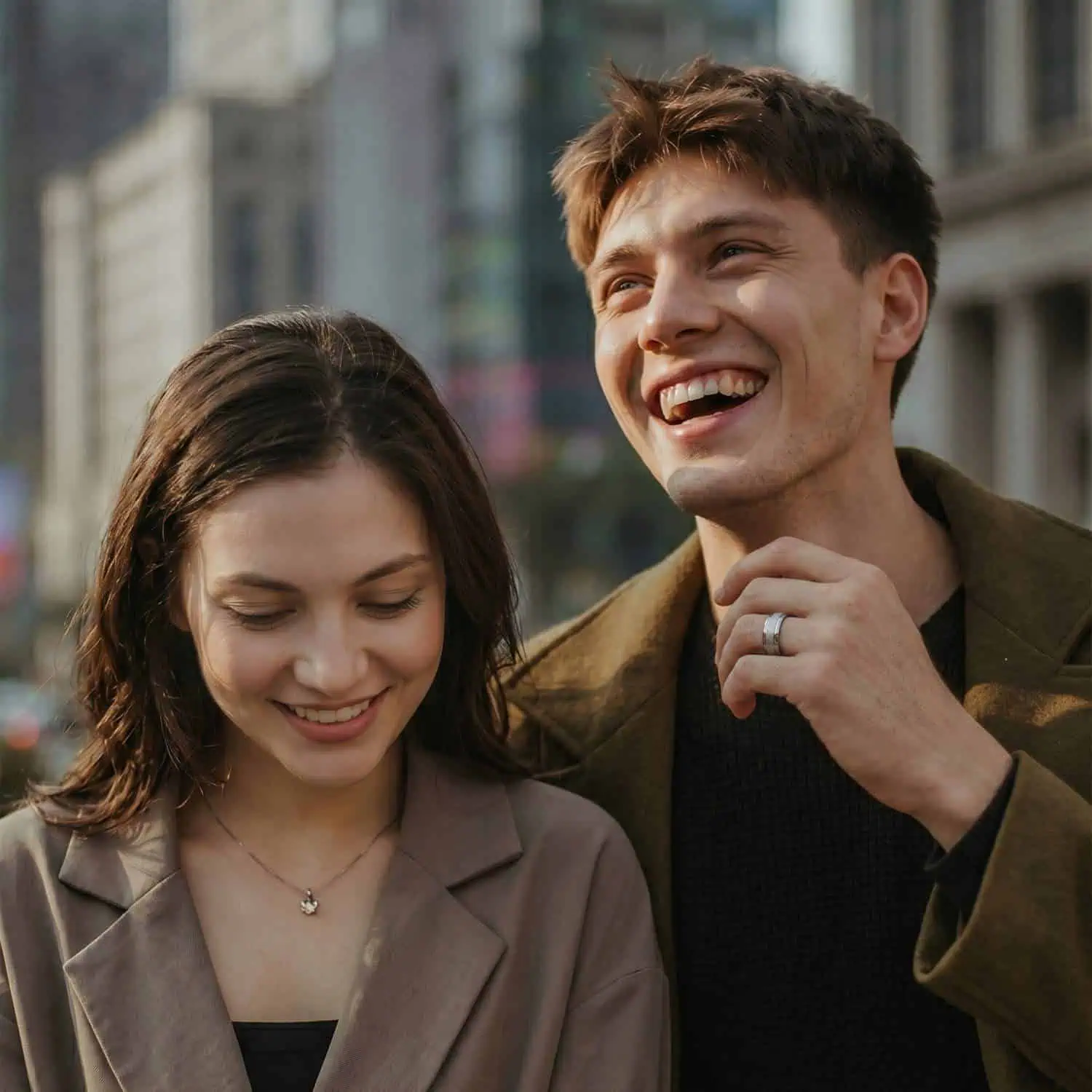 Happy couple sharing a moment with the man wearing the Vantage white gold tungsten wedding band as he laughs with skyscrapers in the background.