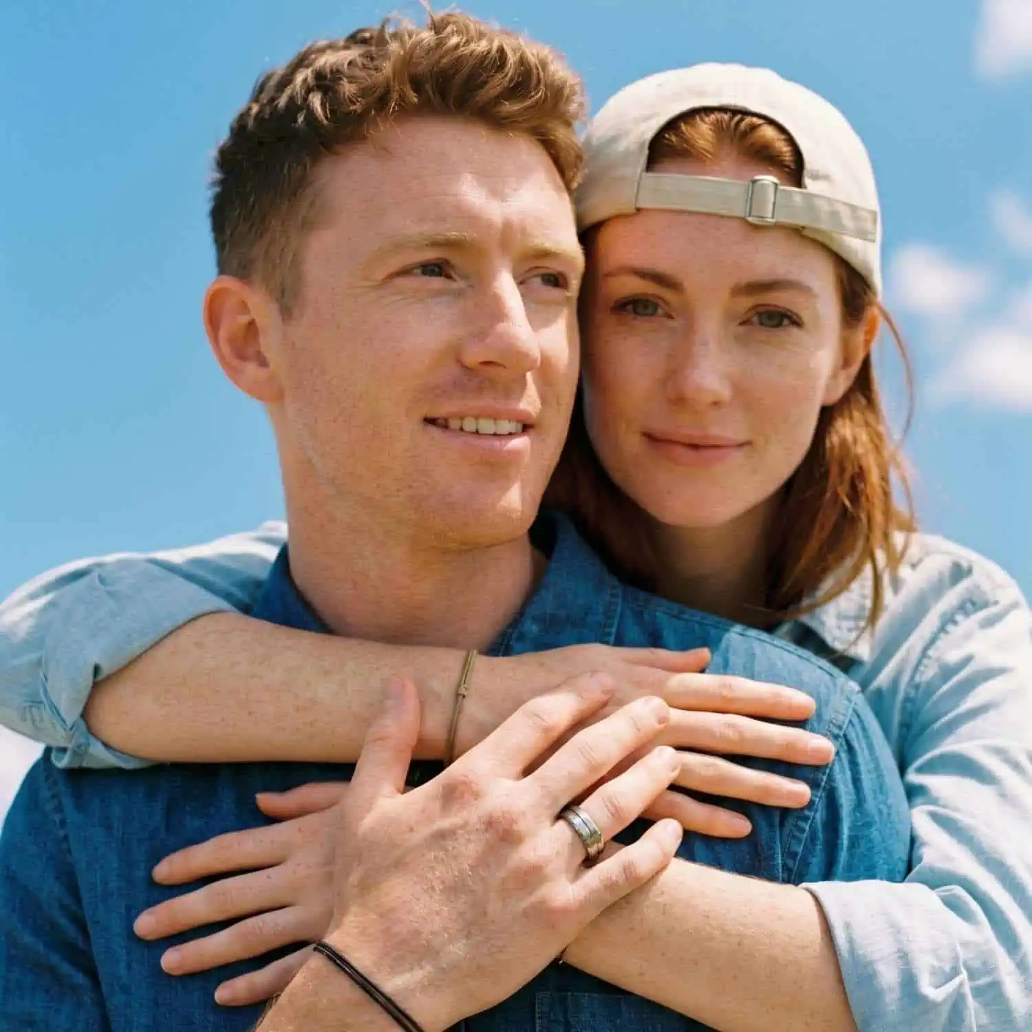 Smiling couple standing together beneath a blue sky with the man wearing the Zenith white gold tungsten wedding band while holding his partner's hand.