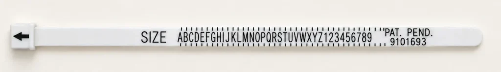 A white plastic strip ring sizer laid flat, marked with sizes A to Z and 1 to 9