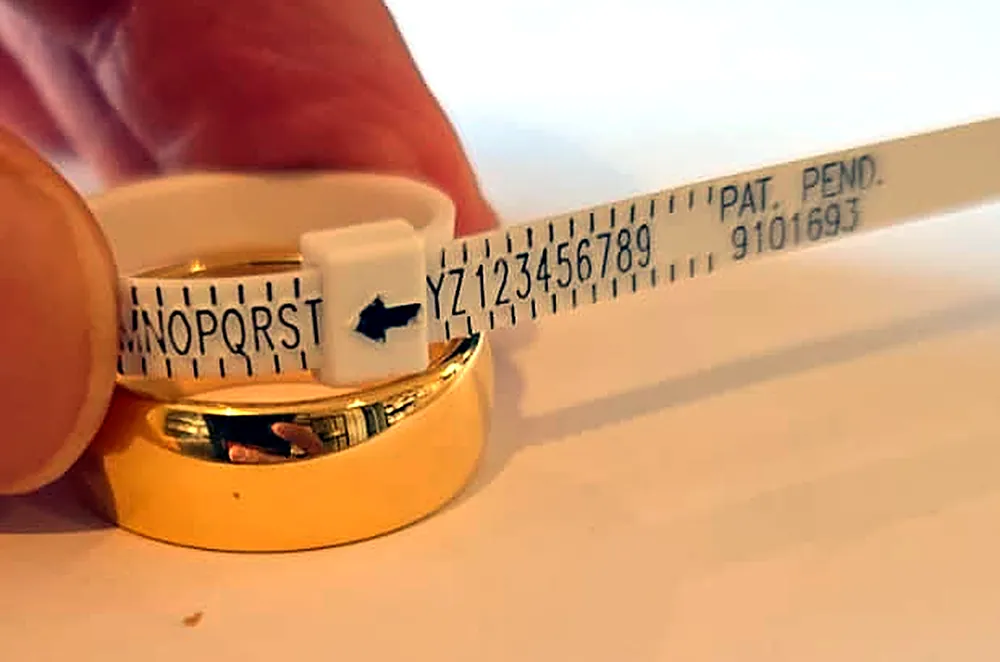 A white strip ring sizer fitted inside a gold tungsten ring, with the arrow pointing to the letter T