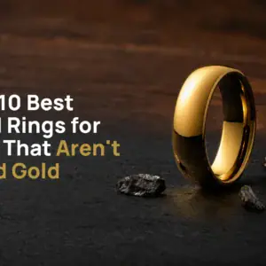The King polished gold-coloured tungsten ring standing on dark slate beside flecks of raw tungsten, with the title The 10 Best Gold Rings for Men That Aren't Solid Gold