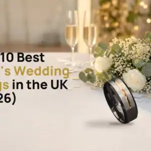 The Champion tungsten ring with a brushed silver-coloured face, rose-gold-coloured groove and black edges on a white wedding table beside a bouquet of white roses and two glasses of champagne, with the title The 10 Best Men's Wedding Rings in the UK (2026)