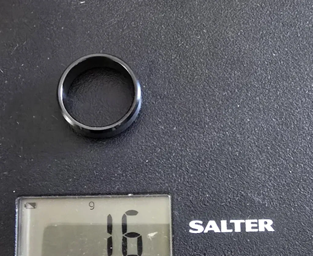 The Strength black tungsten ring with brushed centre and polished bevelled edges on a Salter scale reading 16 g