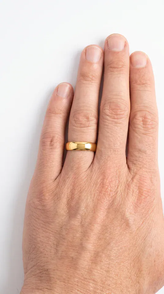 The Graceful polished gold-coloured titanium ring worn on the ring finger of a man's hand on a white studio surface