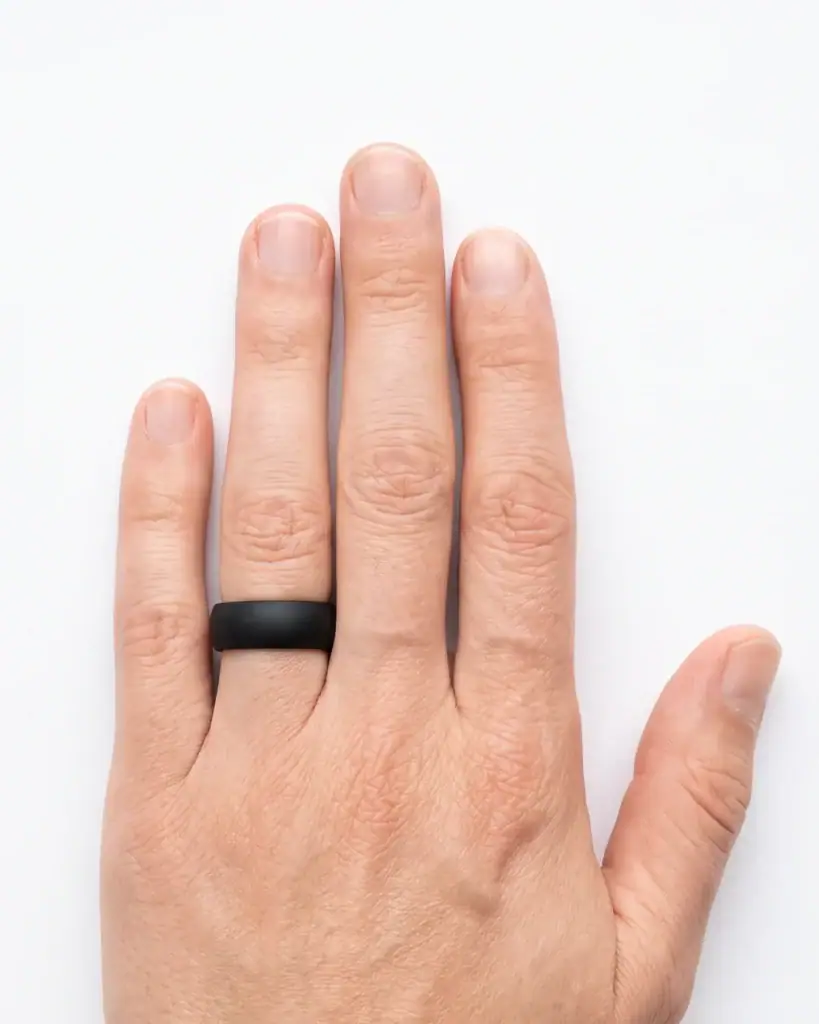 The Kepler black silicone ring worn on the ring finger of a man's left hand on a white studio surface