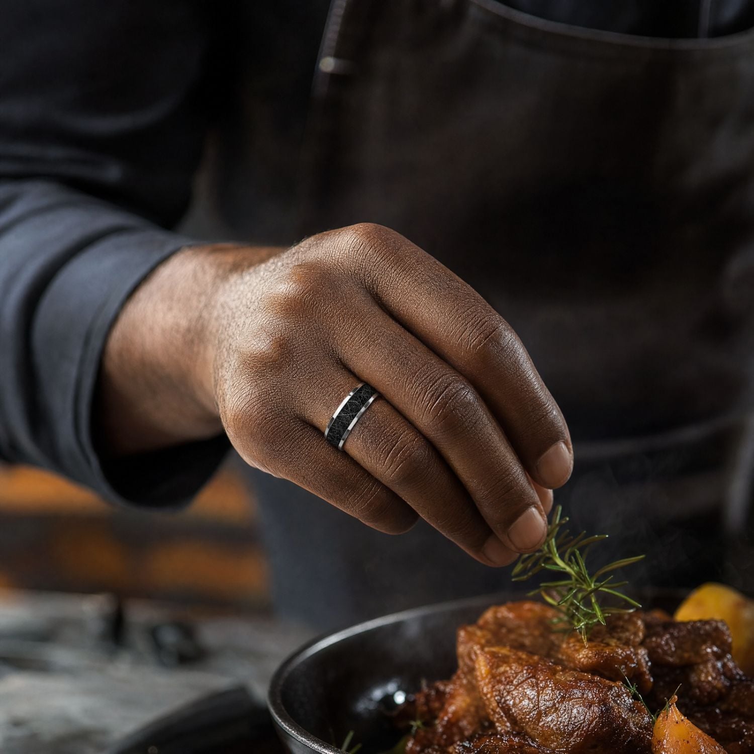 Close-up of a man's hand adding herbs to a meal while wearing a polished silver tungsten ring with a black faux meteorite centre inlay.