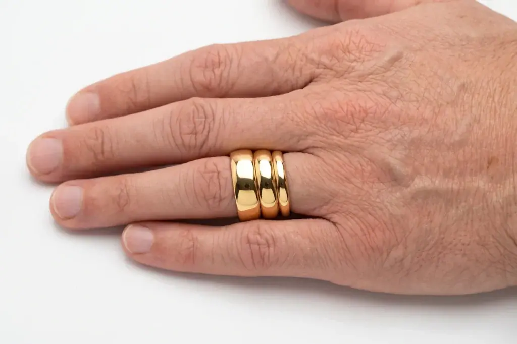 Three gold tungsten rings of 4mm, 6mm and 8mm width worn together on one ring finger, showing the difference in ring width