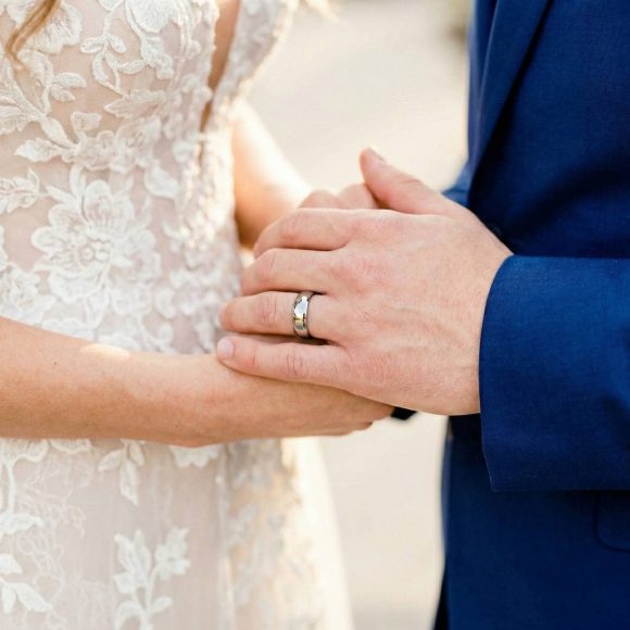 During the wedding ceremony, the newly married couple join hands. The man is wearing his new wedding band which is a polished silver tungsten ring. It is slightly domed in shape and is the style of a classic mens wedding ring.